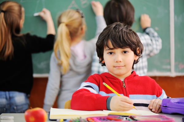 Cute little schoolboy drawing an apple and looking at camera