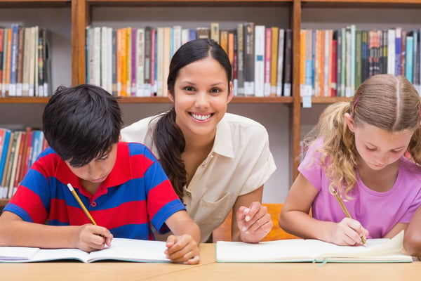 Pretty teacher helping pupils in library at the elementary school